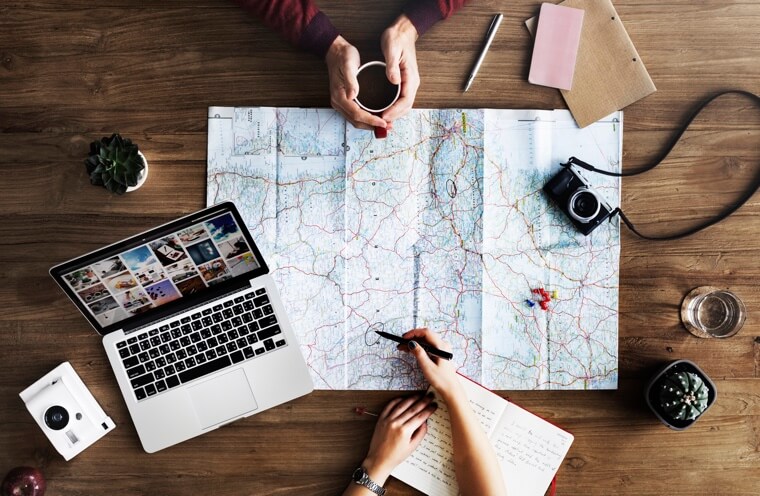 One person traces a route on a map while the other watches and holds a cup of coffee