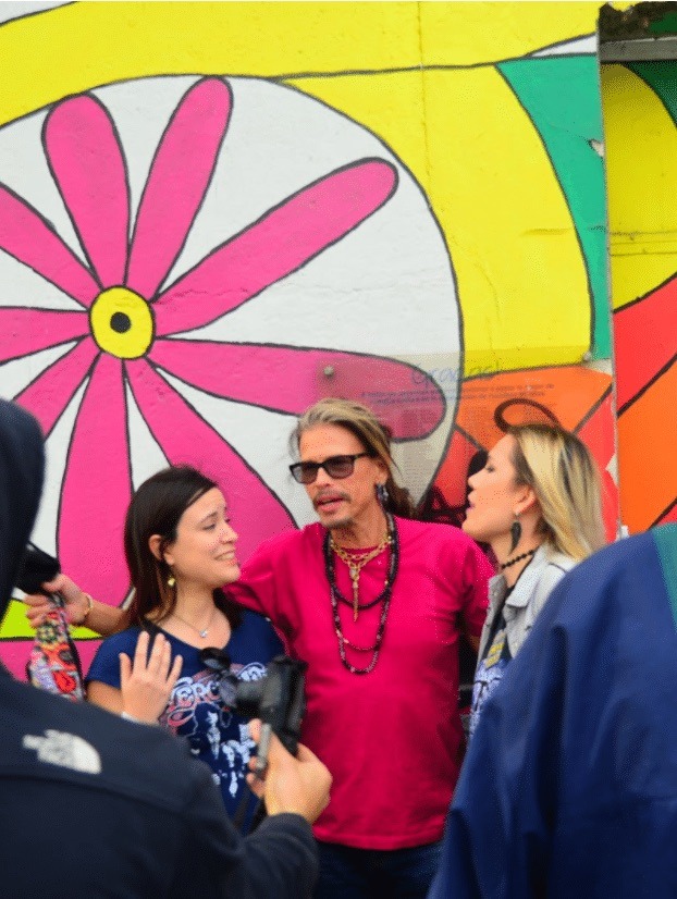 Steven Tyler posing with two women against a floral mural background